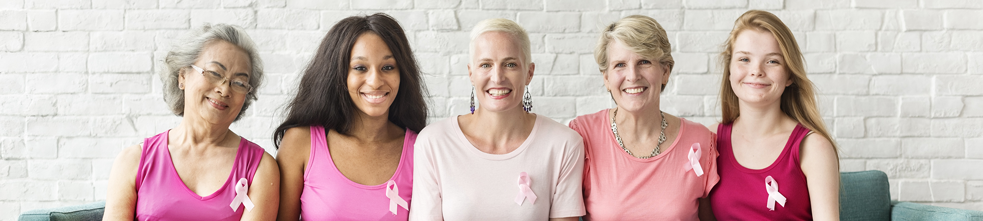 Group of 5 smiling women wearing breast cancer awareness ribbons