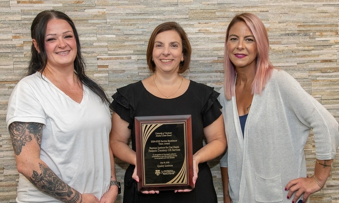 Three women smile holding a plaque that reads