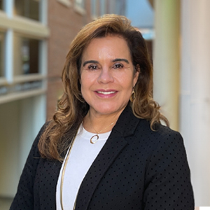 Person standing smiling at camera with long hair wearing white shirt and black blazer
