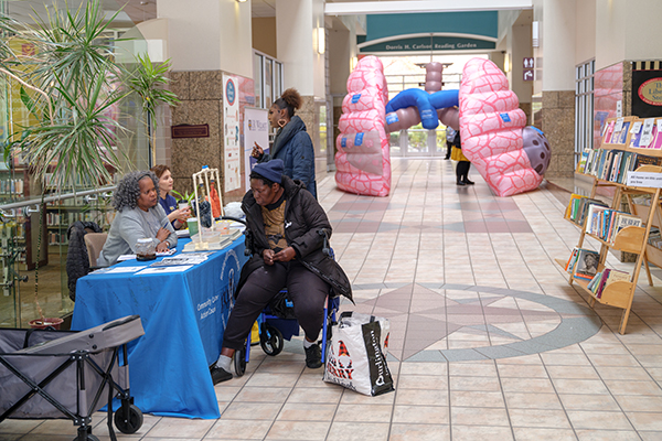 People talk at an information table in a hospital hallway with a large inflatable lung display in the background.