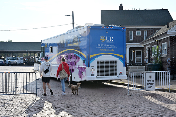 People walk toward a mobile breast imaging van parked outside a building.