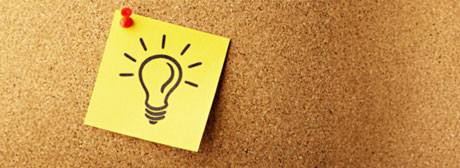 A bulletin board with a post-it note pinned to it with a light bulb drawing on it.