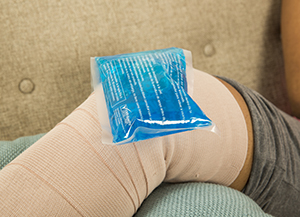 Closeup of knee wrapped in bandage, lying on pillow with ice pack on top