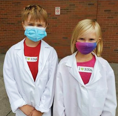 photo of two children wearing masks and white lab coats