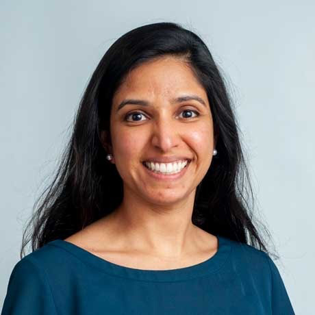person smiling at camera with long dark hair wearing a navy blouse and earings