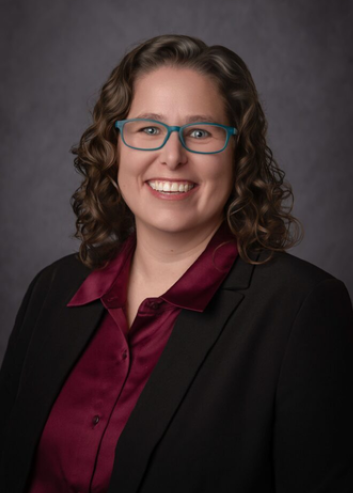 Person smiling at camera, wearing glasses and a black blazer with maroon button down shirt