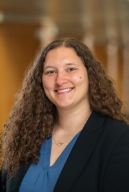 Person with long hair wearing blue shirt and black blazer smiling at camera