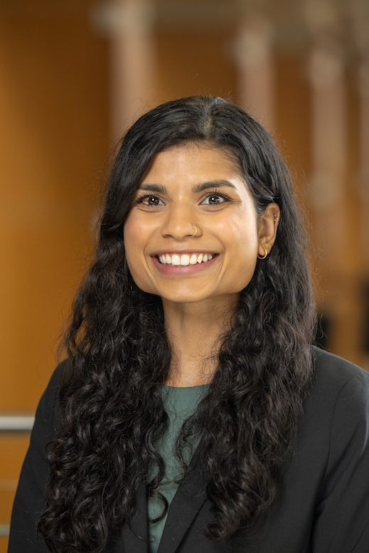 Person with long hair wearing green shirt and black blazer smiling at camera