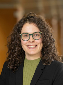 Person with glasses wearing green shirt and black blazer smiling at camera