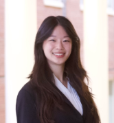 Person with long hair wearing white blouse and black blazer smiling at camera