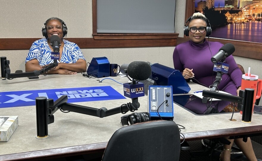 Two individuals sitting around a desk set up for a podcast recording.