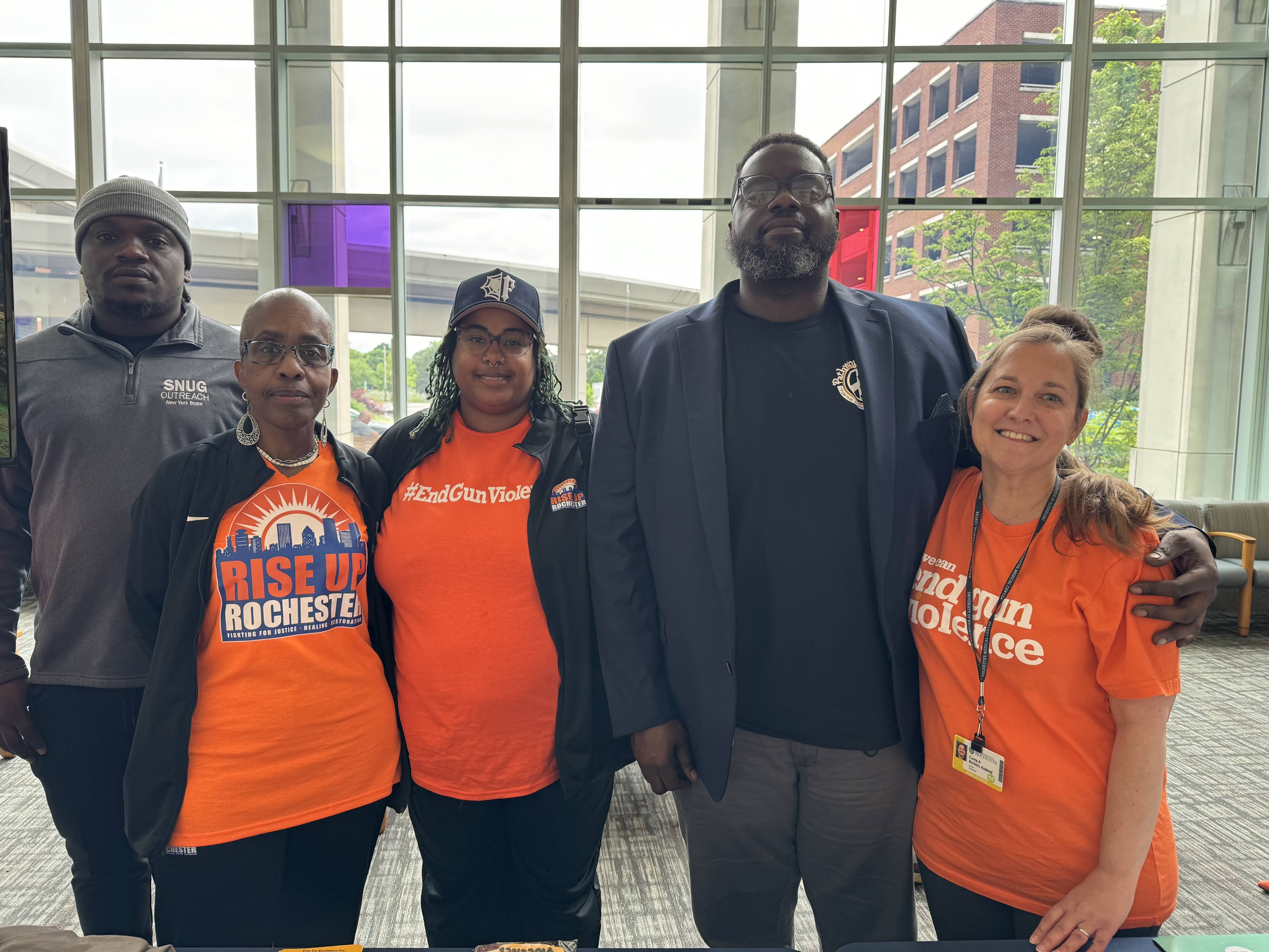 group of five individuals standing together with some wearing Rise Up Rochester and violence prevention shirts.