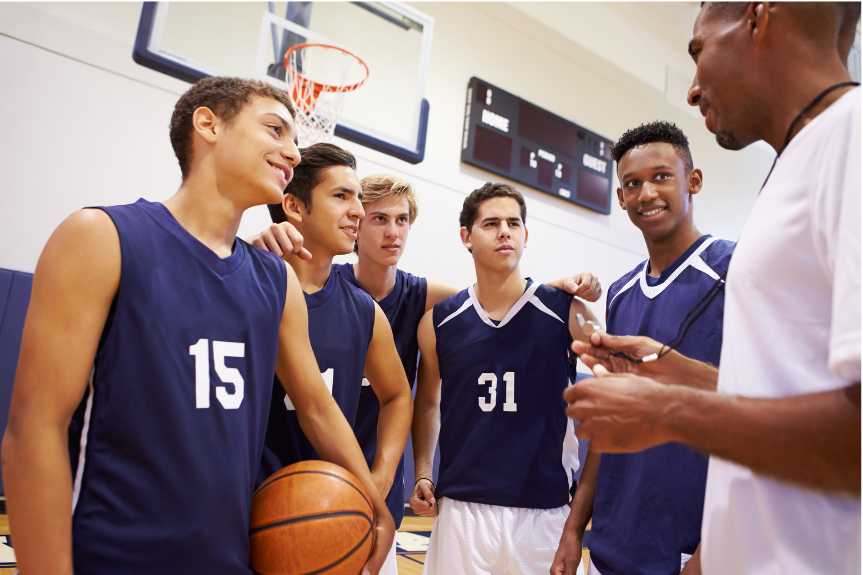group of young men stand on a basketball court talking with coach