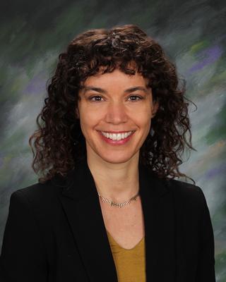 Gretchen Roman wearing a black suit, smiling, curly hair