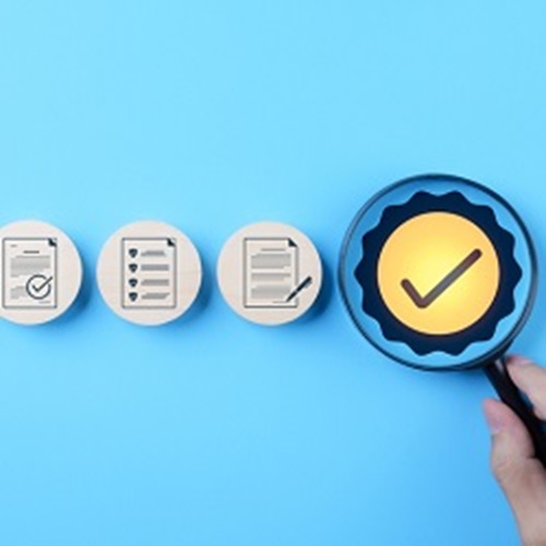 Documents against a blue field with a magnifying glass hovering over yellow badge with checkmark in the center