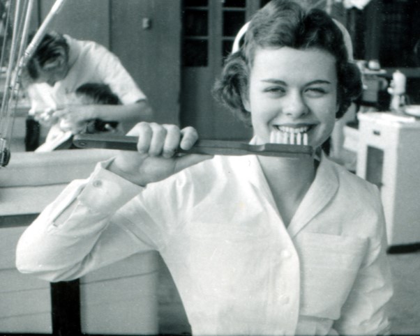 a dental assistant smiles holding an oversized toothbrush