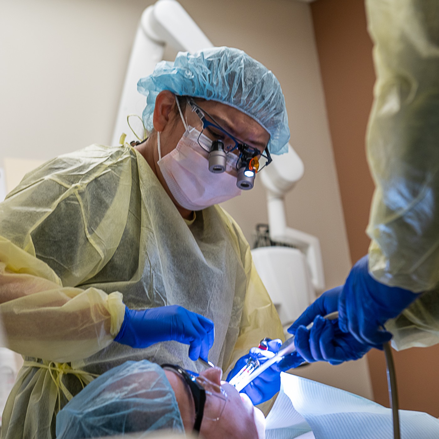 A dentist in full surgical gear treats a patient.