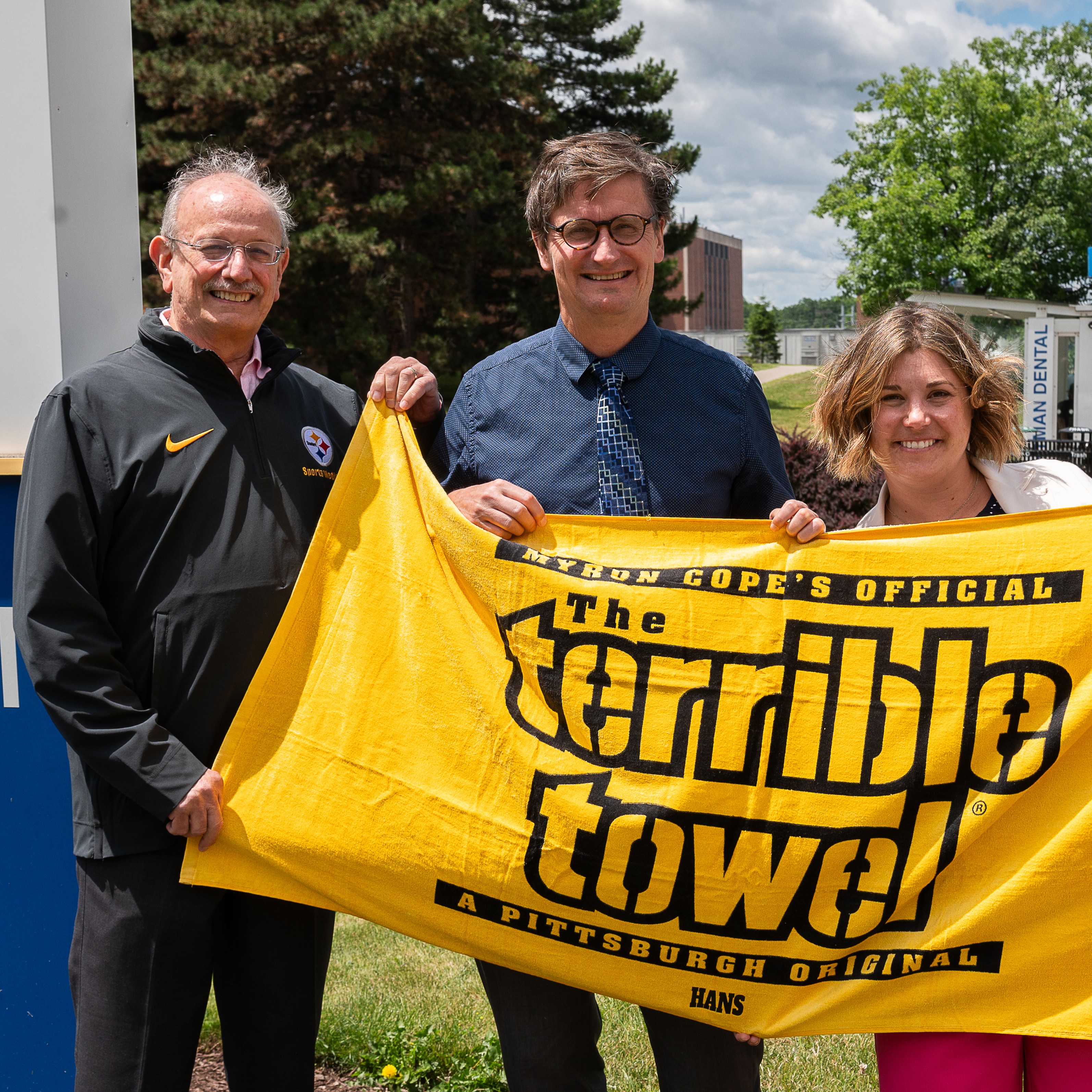 Dr. Gottlieb and two other people hold the Pittsburgh Steelers' Terrible Towel in front of Eastman Dental.