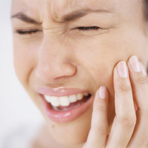face of a person wincing in pain holding cheek/jaw.