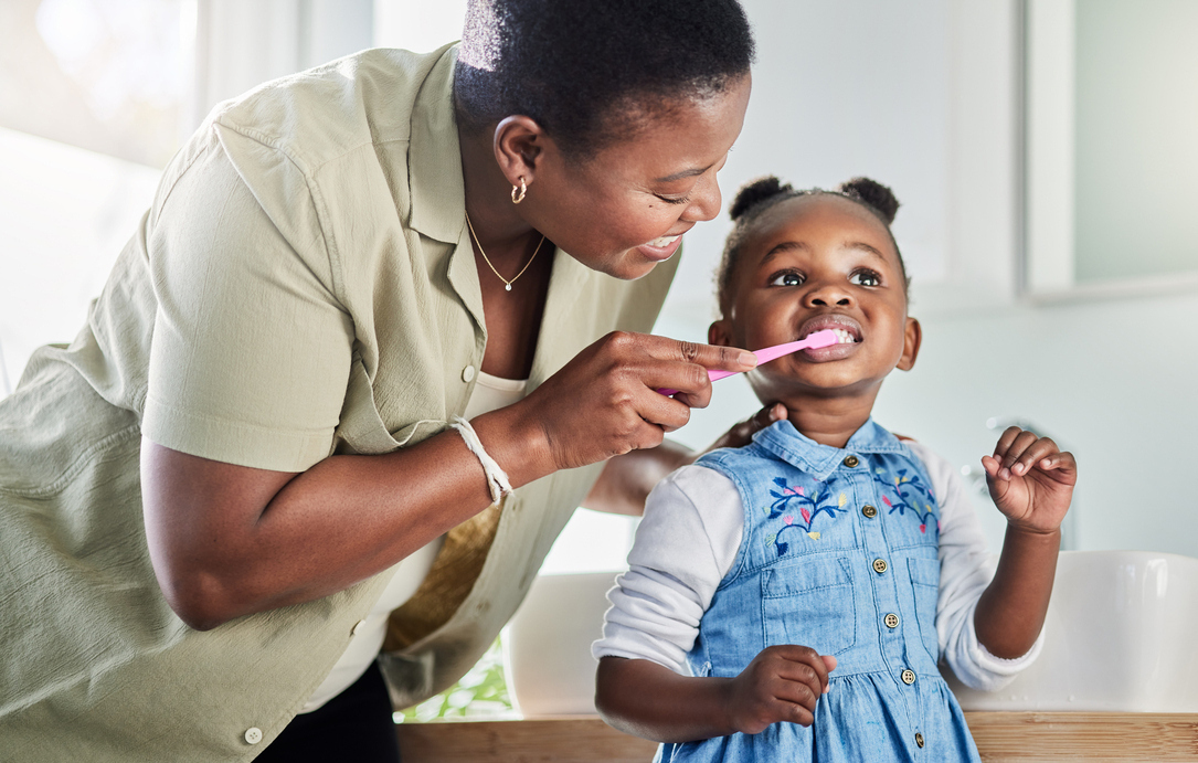 a mother brushes the teeth of a young child