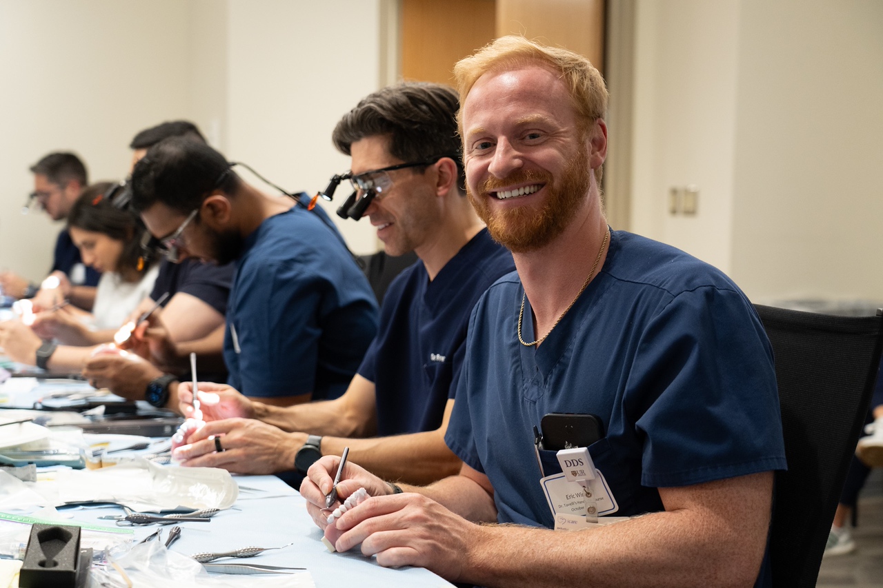 A row of smiling dentists practicing hands-on skills at a workshop.