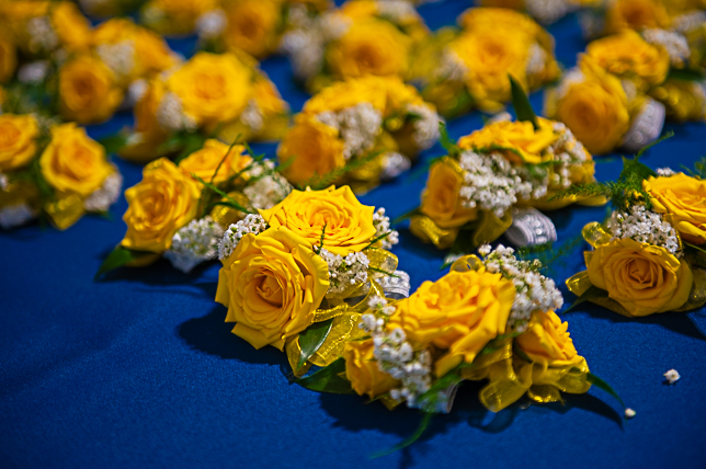 boutonnieres made with yellow roses laid out on a blue table.