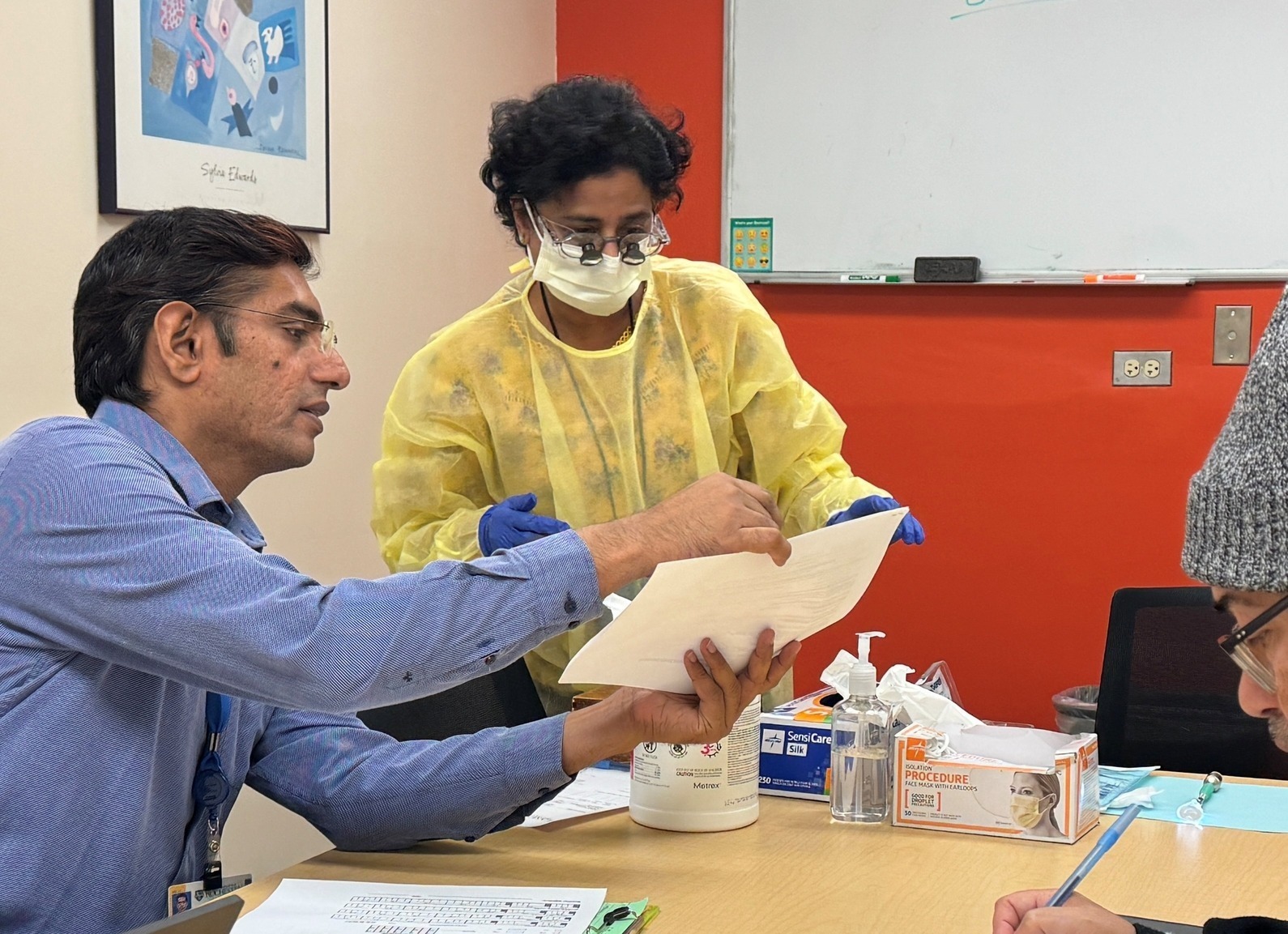 A resident confers with a dentist who is wearing a mask and gloves.