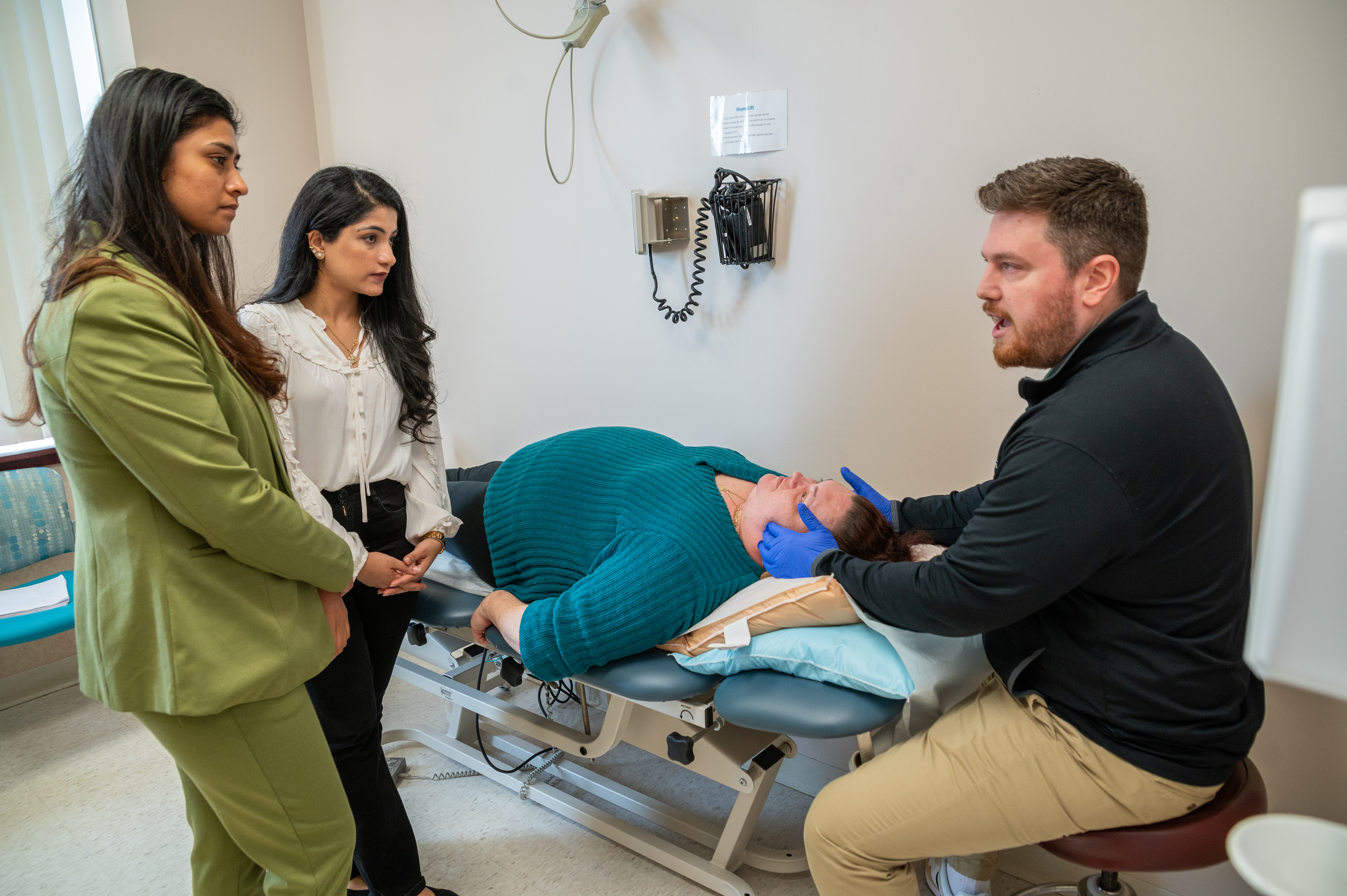 A physical therapist feels a patient's jaw while residents observe.