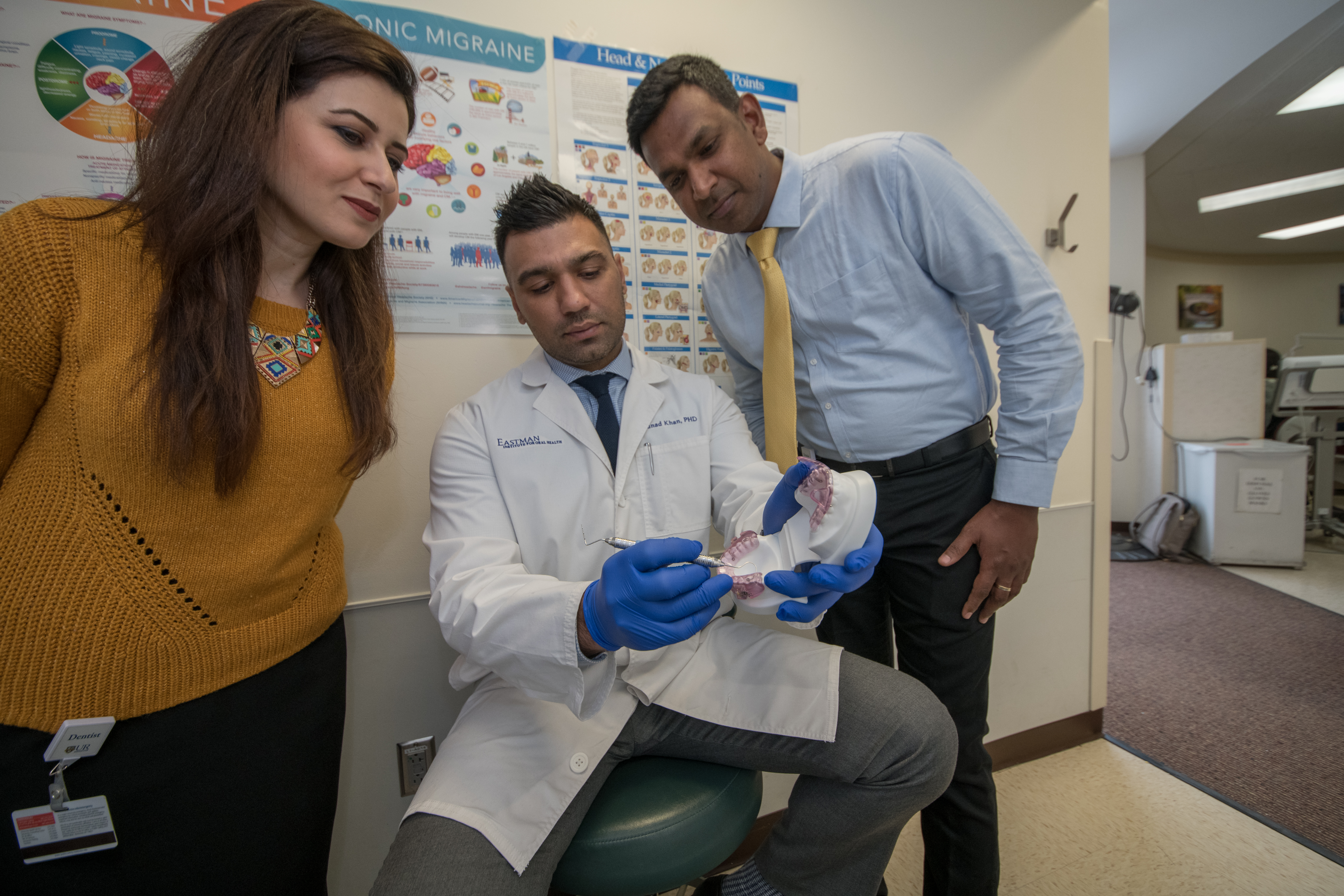 A dentist in a lab coat creates an appliance on a model of a jaw while two residents observe.