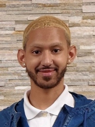 A portrait of Phoenix Rivera, who has light brown skin, a brown beard and moustache, and short-cropped bleached blonde hair.