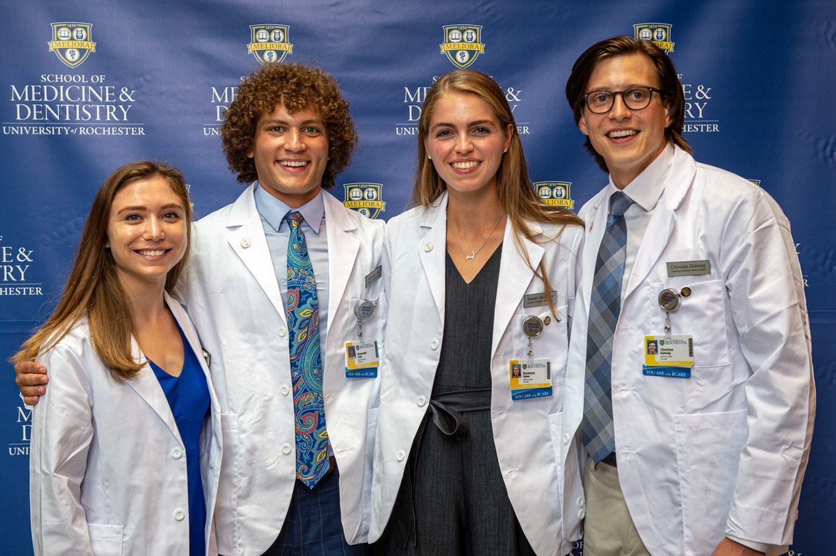 four students stand wearing white coats