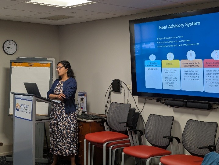 Shalini Beath presenting at the May 2026 Community Advisory Board meeting behind a podium with slide projected behind her