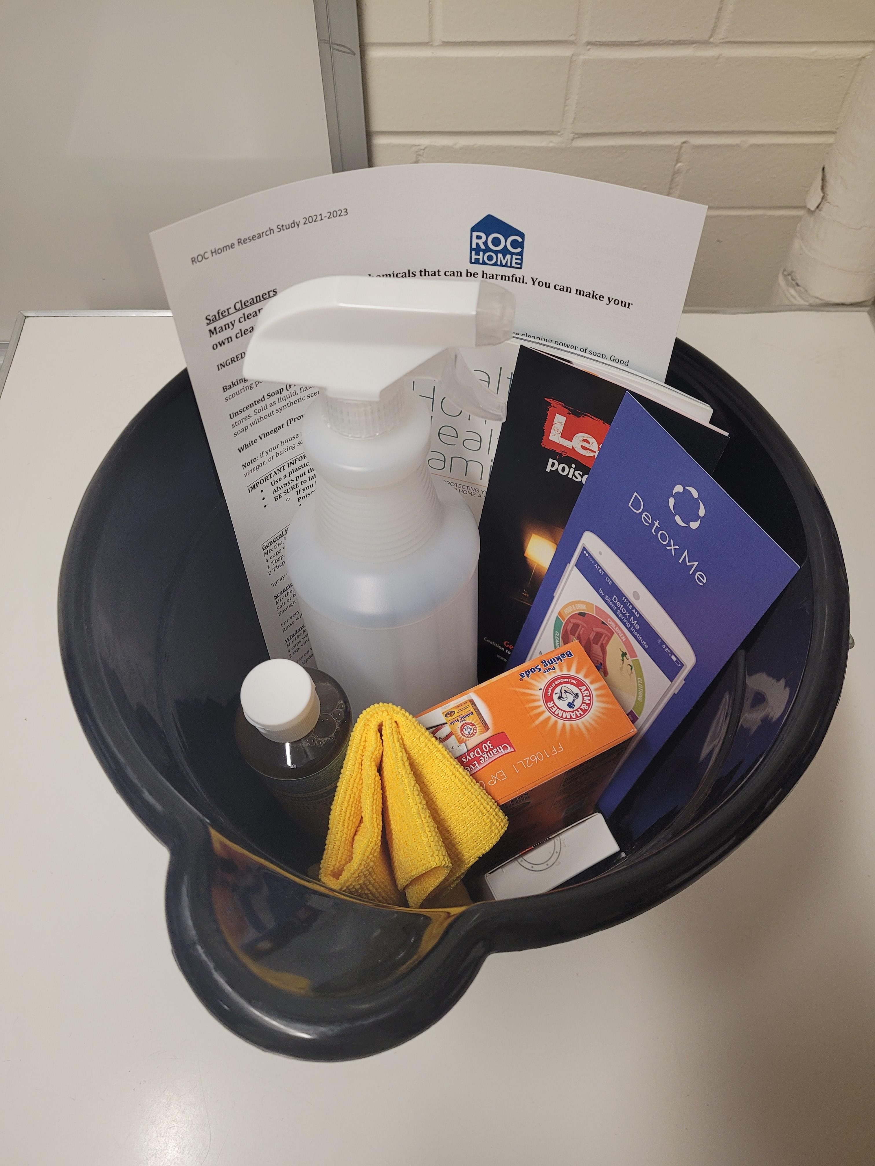 A black cleaning bucket filled with cleaning supplies, a paper towel, and a spray bottle sitting on a counter.