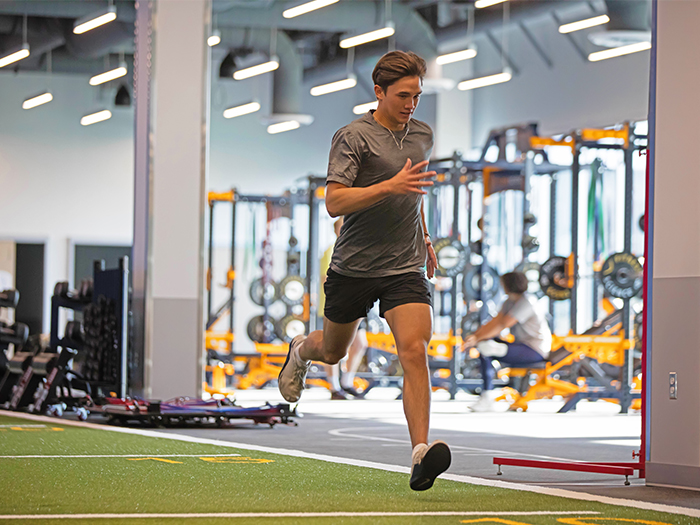 A man is running on in a gym, focused on his workout with exercise equipment in the background..