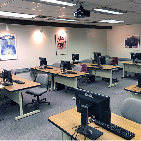Classroom with a ceiling-mounted projector, and several computer workstations facing the front of the room