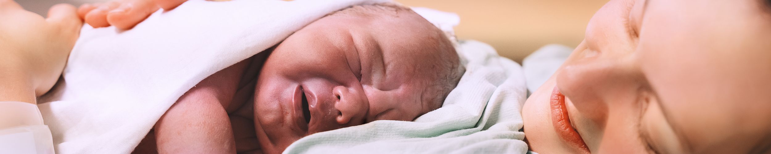 Woman laying with newborn baby on chest wrapped in blanket.