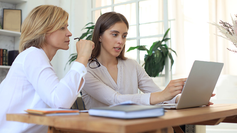 two women discussing information on laptop