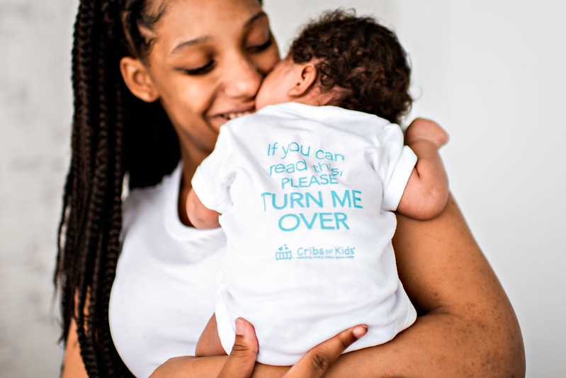 Mother smiling happily and holding baby close on her shoulder.