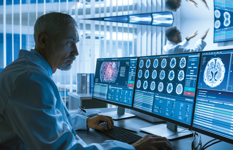 A medical professional looks at brain scan images on multiple computer screens.