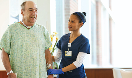 Male patient standing with a female nurse assisting in a hospital room