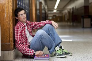 Young man sitting against a wall in school hallway.