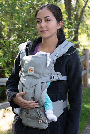 Woman with baby in front carrier walking outdoors.