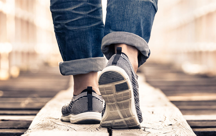 A person in sneakers strolls across a wooden bridge, enjoying the outdoors.