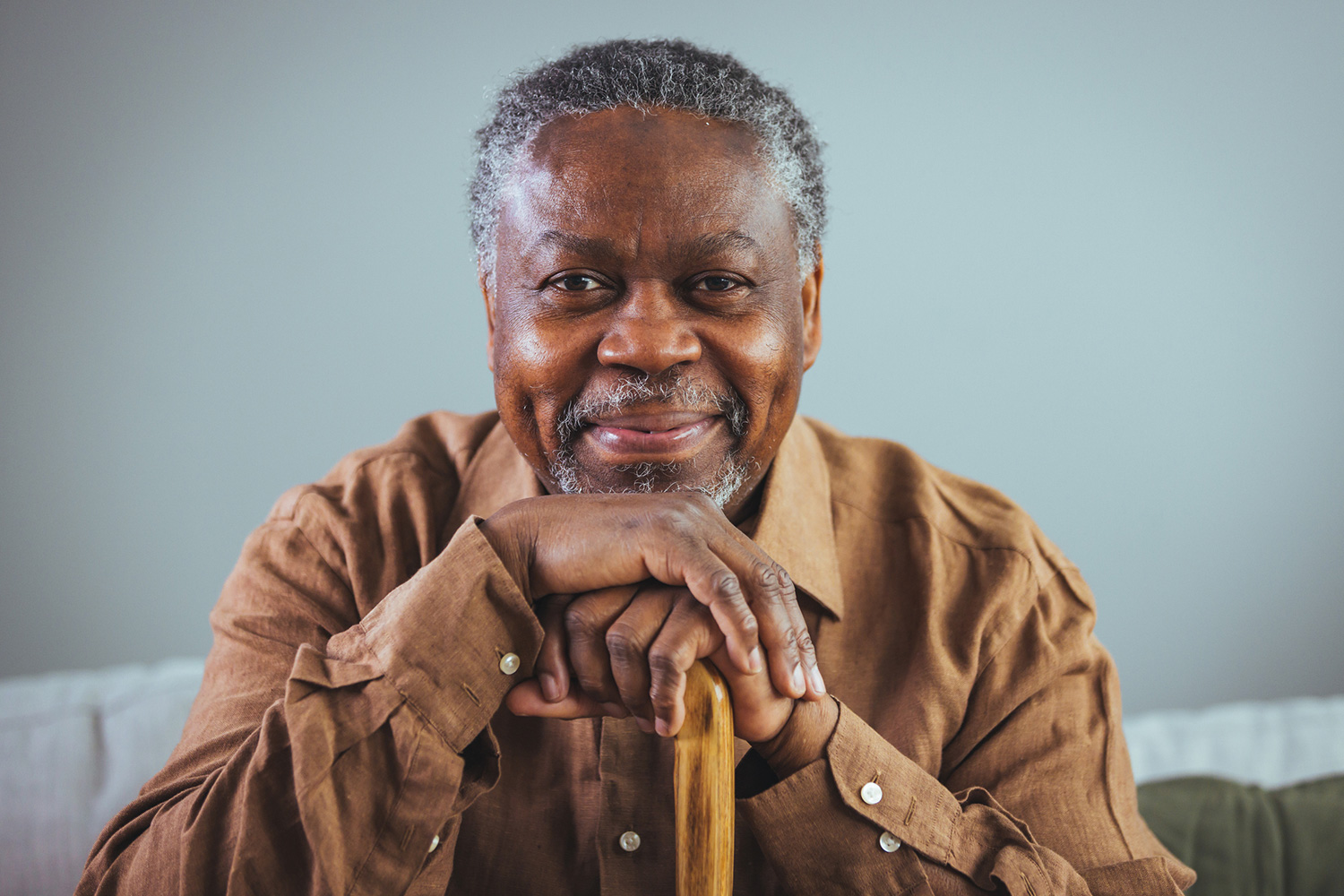Elderly man smiling at the camera, slightly leaning on his cane while seated