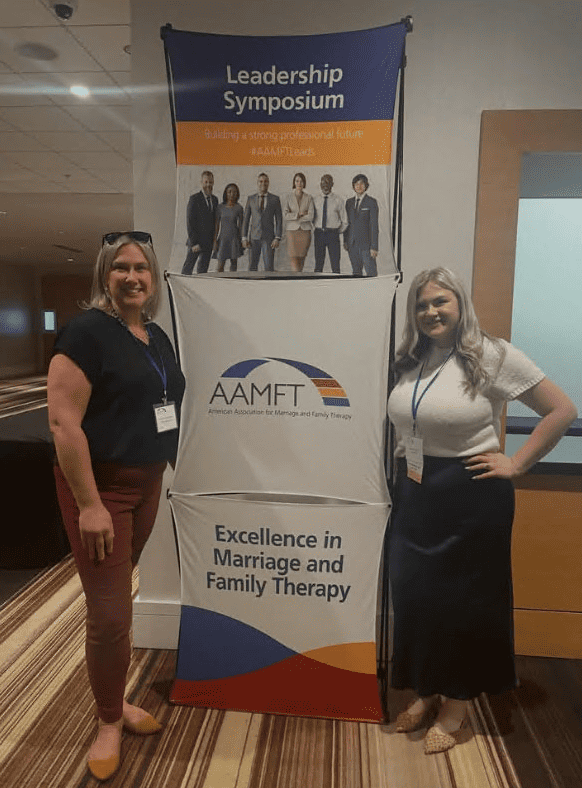 Kristin Koberstein and Gabrielle Gebel in front of a AAMFT banner
