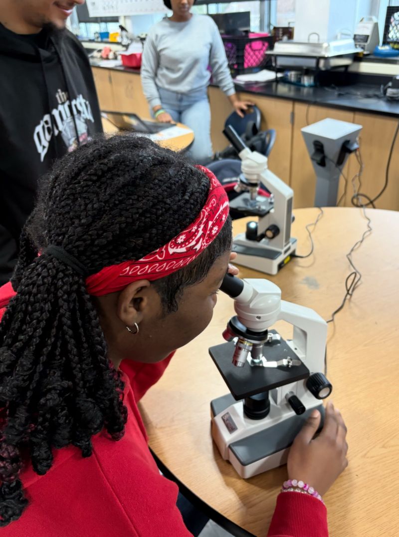 East High student sitting at a table looking through a micrscope