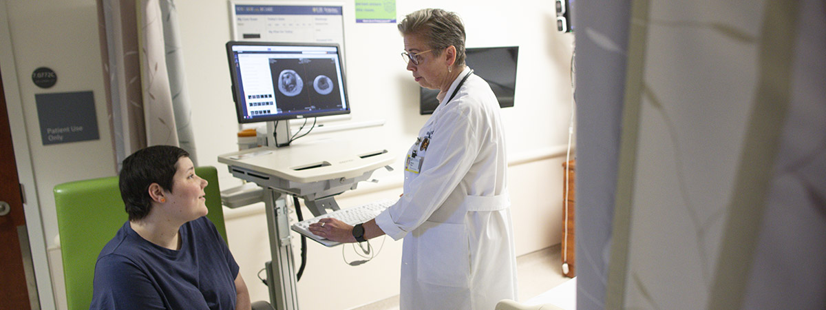 Dr. Marcia Krebs, a hospitalist at Wilmot Cancer Center and professor of Clinical Medicine in the Division of Hematology/Oncology, speaks with her patient, Sarah Moore. Imaging can be seen in the background on a computer screen.